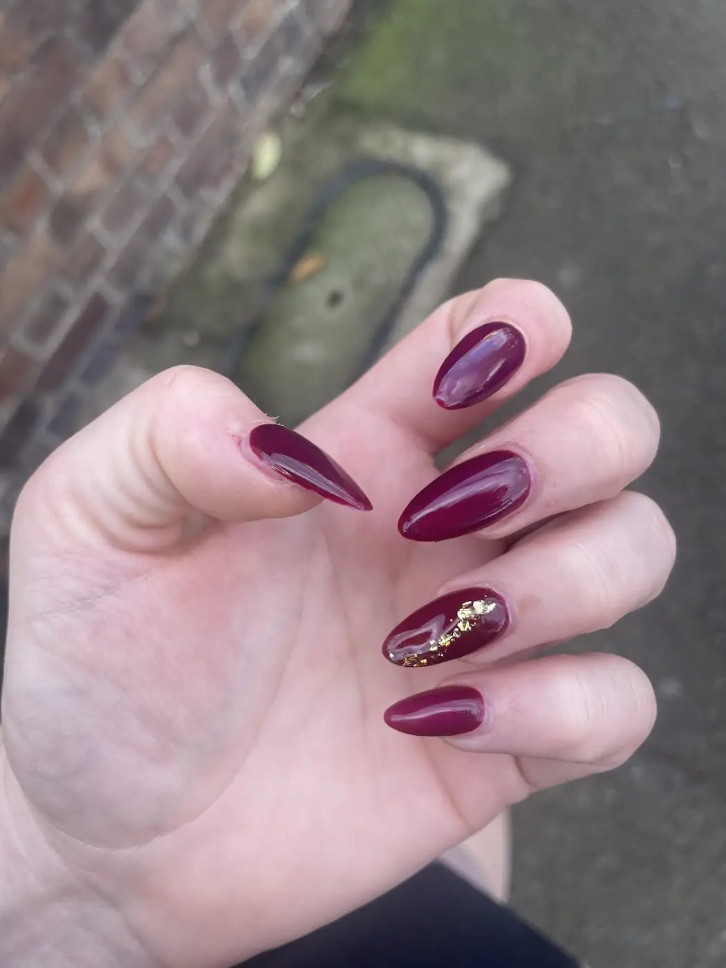 Glossy burgundy almond nails with a gold-flake accent nail